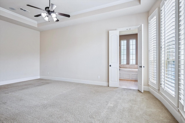 unfurnished room with light colored carpet, crown molding, ceiling fan, a tray ceiling, and baseboards
