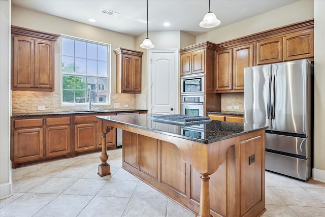 kitchen featuring appliances with stainless steel finishes, a sink, a center island, dark stone counters, and light tile patterned flooring