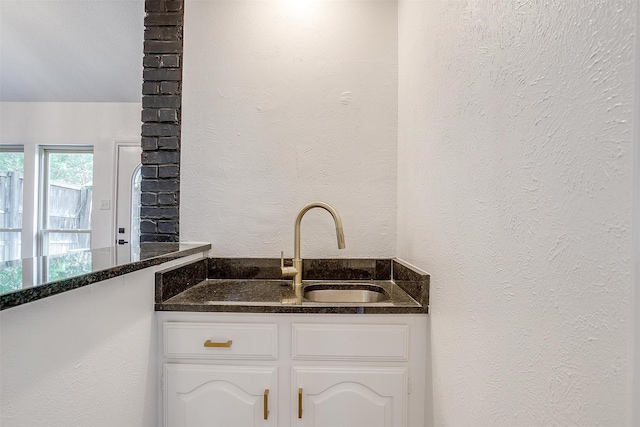 2204 Mediterranean Ave, Arlington, TX 76011 - kitchen featuring white cabinets, a sink, dark stone counters, and a textured wall