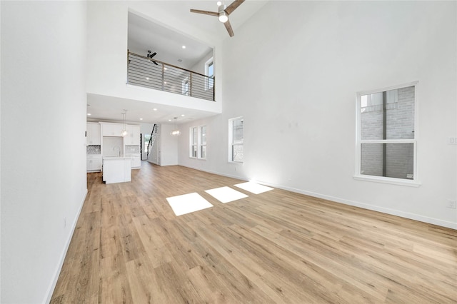 220 E Park St, Little Elm, TX 75068 - unfurnished living room featuring a high ceiling, light wood-style flooring, a ceiling fan, baseboards, and a sink