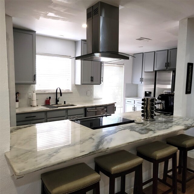 15642 Overmead Cir, Dallas, TX 75248 - kitchen featuring island exhaust hood, a sink, backsplash, gray cabinets, and light stone countertops