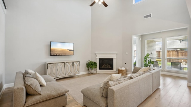 4190 Sandhills Ln, Prosper, TX 75078 - living area with ceiling fan, light wood-type flooring, a glass covered fireplace, a high ceiling, and baseboards