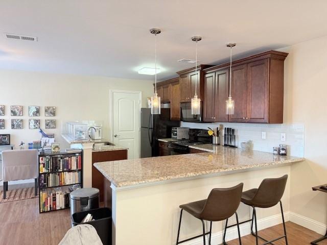 5616 Preston Oaks Rd Unit 110, Dallas, TX 75254 - kitchen featuring black appliances, a peninsula, light wood-type flooring, a kitchen bar, and a sink