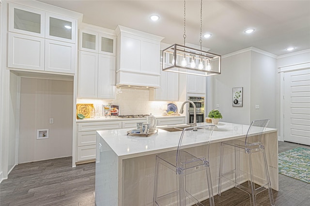 3928 Hogan Dr, Tyler, TX 75709 - kitchen with dark wood-style floors, white cabinetry, backsplash, a center island with sink, and ornamental molding