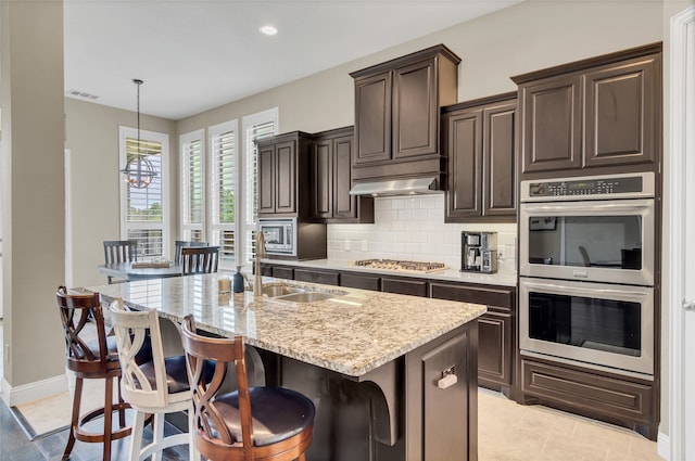 9012 Terrel St, Lantana, TX 76226 - kitchen with stainless steel appliances, light stone countertops, tasteful backsplash, dark brown cabinetry, and a kitchen island with sink