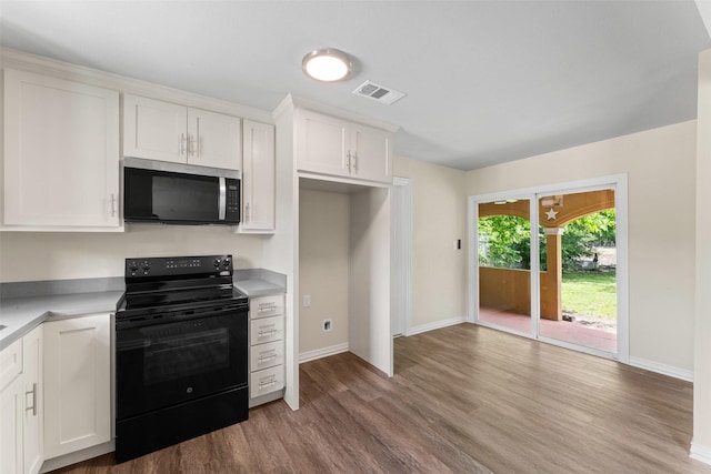 1008 Pleasant Dr, Dallas, TX 75217 - kitchen featuring stainless steel microwave, black range with electric stovetop, wood finished floors, and white cabinetry