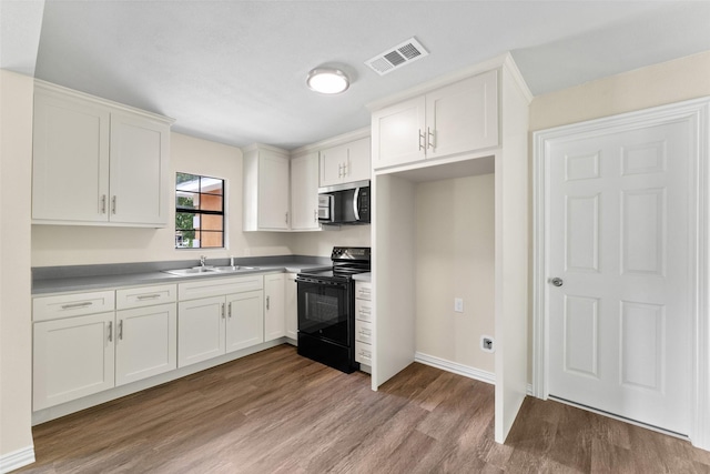 1008 Pleasant Dr, Dallas, TX 75217 - kitchen featuring black / electric stove, stainless steel microwave, wood finished floors, a sink, and white cabinets