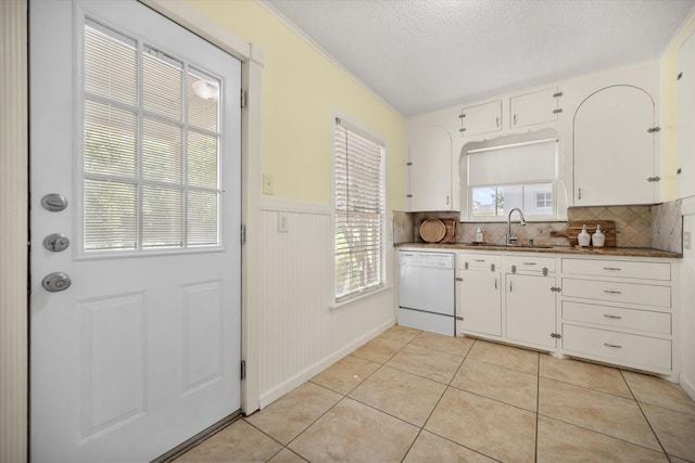 kitchen with white dishwasher, a sink, white cabinets, a textured ceiling, and decorative backsplash