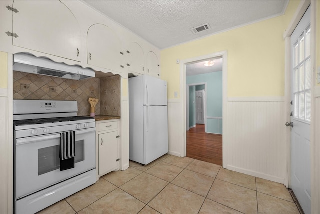 kitchen featuring white appliances, under cabinet range hood, white cabinetry, tasteful backsplash, and light tile patterned floors