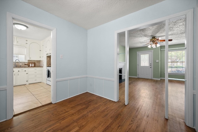 empty room featuring a textured ceiling, a ceiling fan, wood finished floors, a sink, and a fireplace