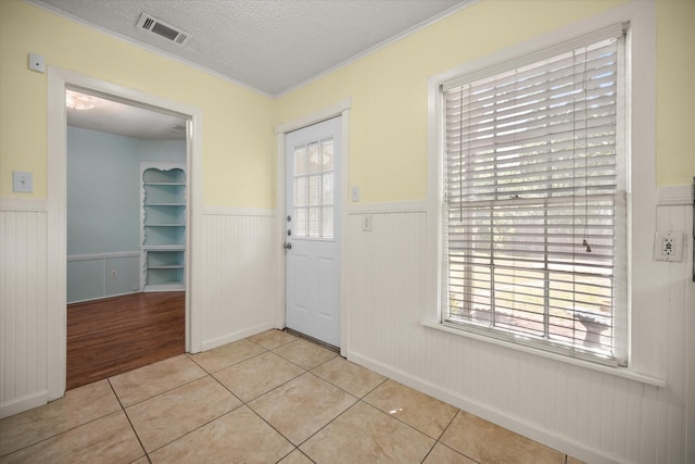 foyer featuring a wainscoted wall, a textured ceiling, light tile patterned flooring, and ornamental molding