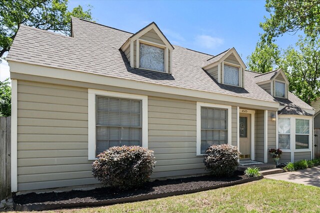 cape cod home with a front yard and a shingled roof