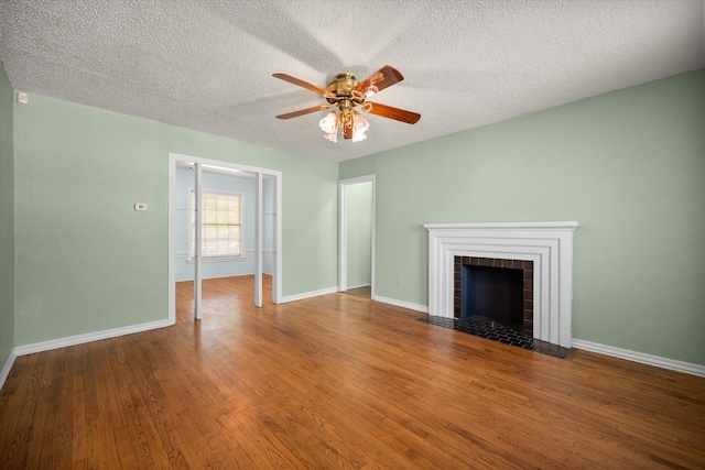 unfurnished living room featuring ceiling fan, wood finished floors, a tile fireplace, a textured ceiling, and baseboards