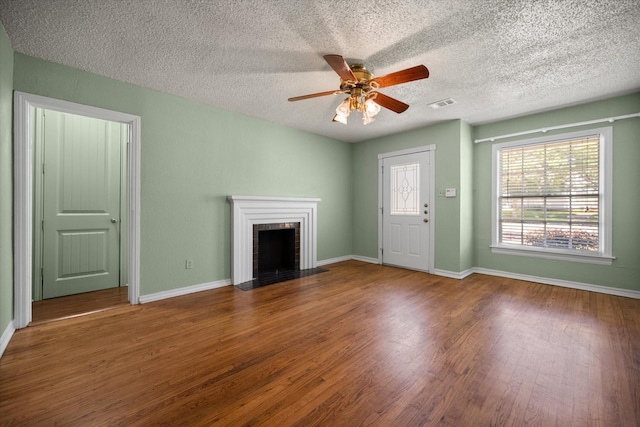 unfurnished living room with wood finished floors, ceiling fan, a fireplace, baseboards, and a textured ceiling