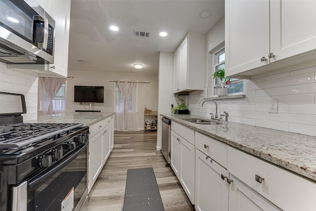 3444 Kellogg Ave, Dallas, TX 75216 - kitchen with stainless steel appliances, a sink, white cabinetry, light wood-style flooring, and tasteful backsplash