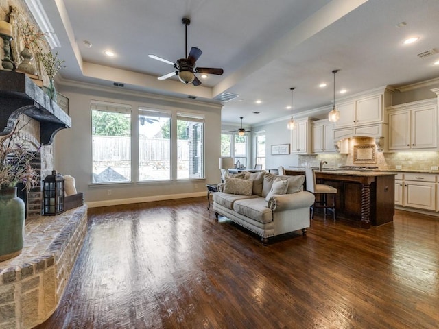 114 Crestbrook Dr, Rockwall, TX 75087 - living area with a ceiling fan, dark wood-style floors, ornamental molding, a stone fireplace, and a tray ceiling
