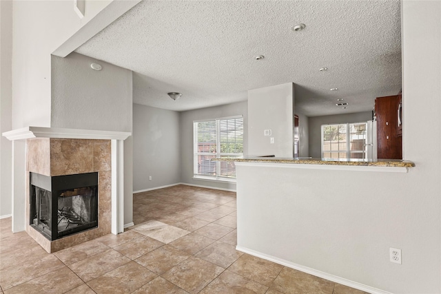 unfurnished living room featuring a textured ceiling, healthy amount of natural light, a fireplace, light tile patterned floors, and baseboards