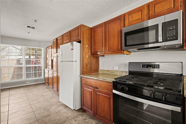 kitchen with stainless steel appliances, brown cabinets, light tile patterned flooring, light stone counters, and a textured ceiling