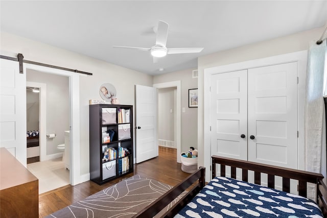 9031 Fringewood Dr, Dallas, TX 75228 - bedroom with a barn door, dark wood-type flooring, a closet, connected bathroom, and ceiling fan