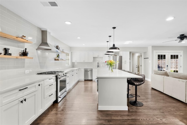 9031 Fringewood Dr, Dallas, TX 75228 - kitchen featuring appliances with stainless steel finishes, wall chimney range hood, tasteful backsplash, open floor plan, and a kitchen breakfast bar