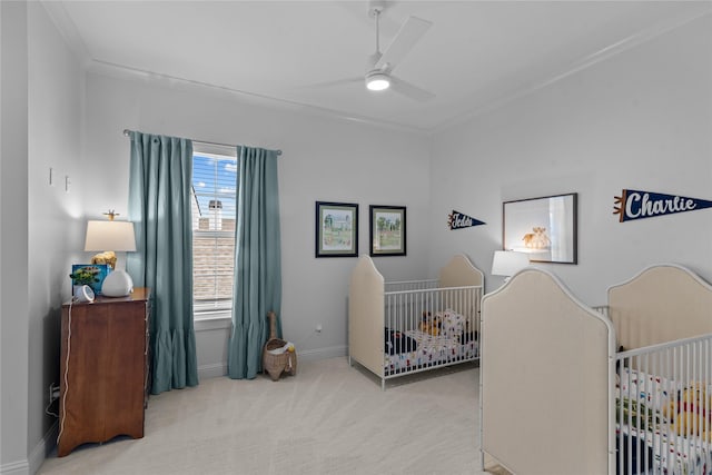 carpeted bedroom with baseboards, a crib, and ceiling fan