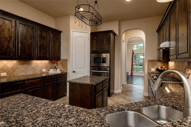 604 Carnaby Ct, Roanoke, TX 76262 - kitchen featuring a sink, arched walkways, appliances with stainless steel finishes, dark stone countertops, and dark brown cabinets