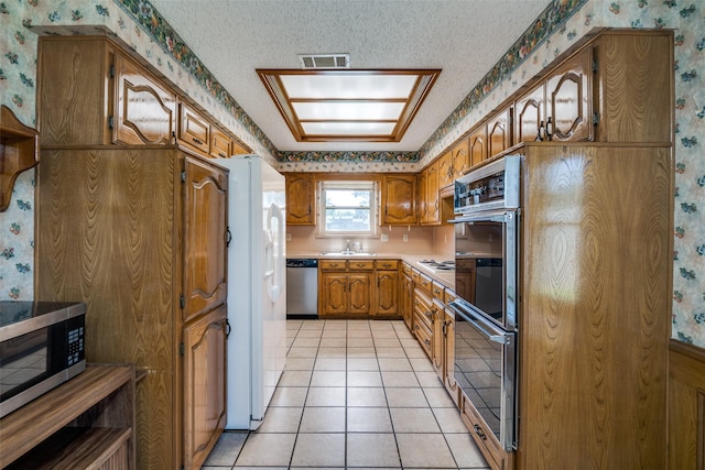 3506 Carla Dr, Rowlett, TX 75088 - kitchen featuring wallpapered walls, appliances with stainless steel finishes, brown cabinets, light countertops, and light tile patterned floors