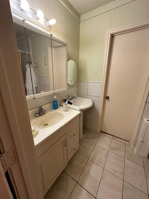 301 Dogwood Ave, Princeton, TX 75407 - bathroom featuring a textured ceiling, tile patterned floors, a wainscoted wall, vanity, and tile walls