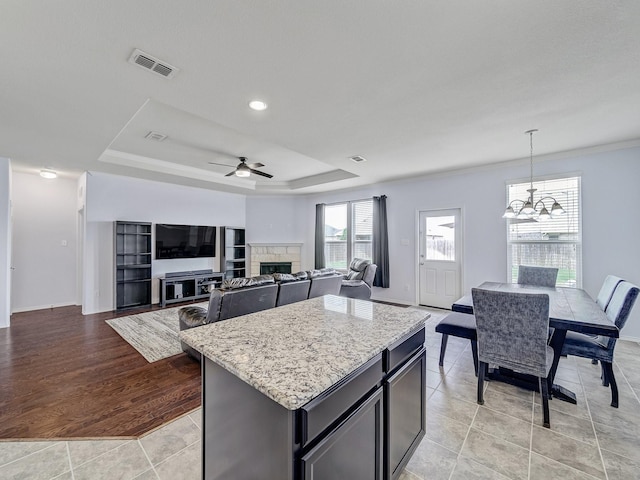 905 Jonius Creek Dr, Little Elm, TX 75068 - kitchen with a stone fireplace, a kitchen island, a tray ceiling, light tile patterned flooring, and recessed lighting