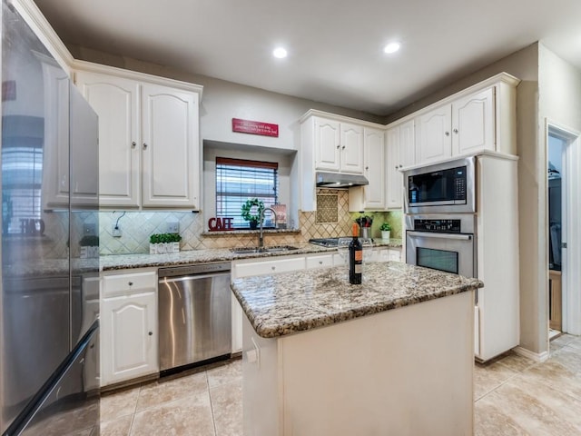kitchen featuring appliances with stainless steel finishes, under cabinet range hood, a sink, light stone counters, and white cabinetry