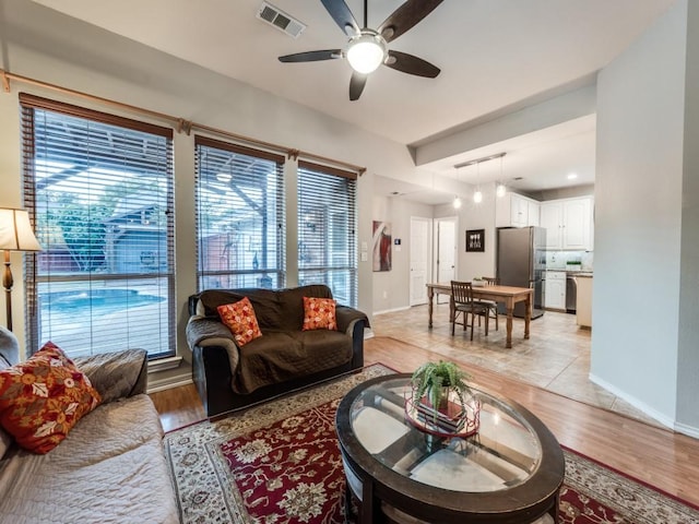 living area featuring ceiling fan, healthy amount of natural light, baseboards, and light wood-type flooring