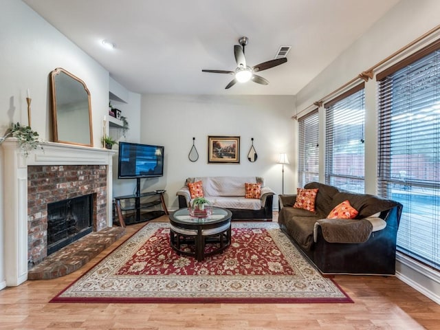 living room with healthy amount of natural light, a ceiling fan, wood finished floors, and a brick fireplace