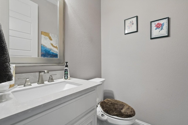 half bath with vanity, a textured wall, and toilet