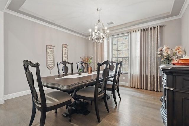 dining space with a chandelier, light wood-style flooring, baseboards, a tray ceiling, and crown molding
