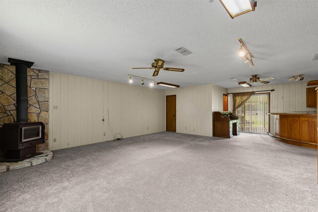 4611 Francis Ct, Granbury, TX 76049 - unfurnished living room featuring track lighting, ceiling fan, a wood stove, a textured ceiling, and wooden walls