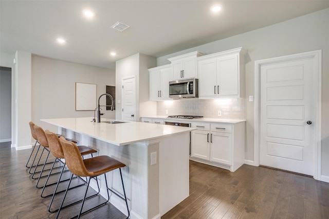 kitchen with a sink, appliances with stainless steel finishes, dark wood-type flooring, an island with sink, and a breakfast bar area