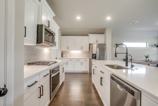 kitchen featuring appliances with stainless steel finishes, a sink, white cabinets, decorative backsplash, and dark wood-type flooring