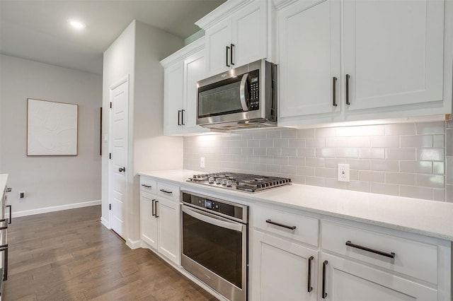 kitchen featuring appliances with stainless steel finishes, white cabinets, baseboards, dark wood-style flooring, and backsplash