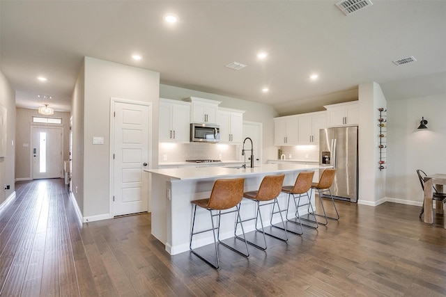 kitchen featuring appliances with stainless steel finishes, a sink, a kitchen island with sink, light countertops, and recessed lighting