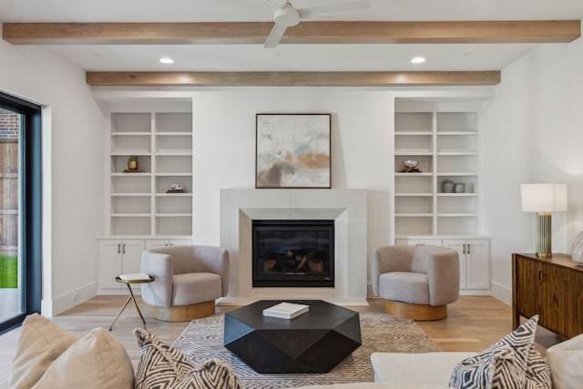 living area featuring light wood-style flooring, beam ceiling, a glass covered fireplace, baseboards, and recessed lighting