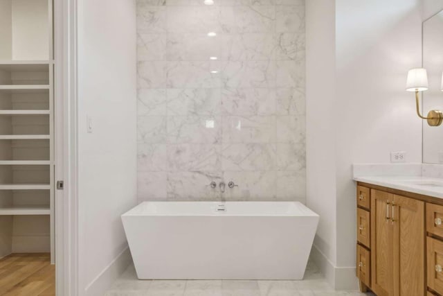 full bath featuring vanity, baseboards, a soaking tub, and a spacious closet
