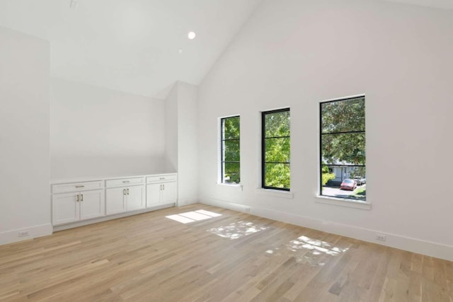 empty room with high vaulted ceiling, baseboards, light wood finished floors, and recessed lighting