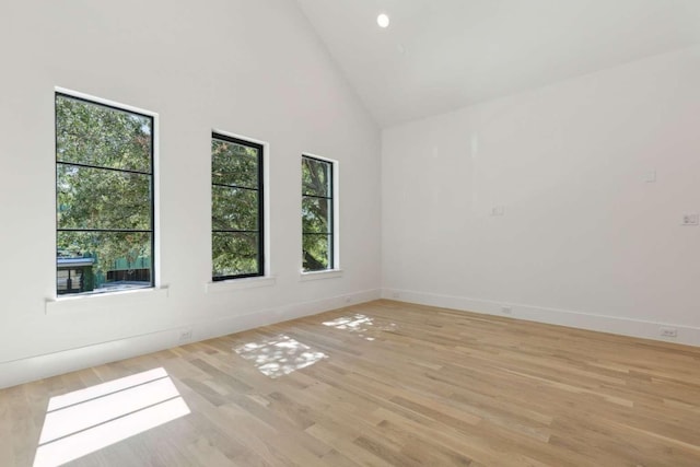unfurnished room with light wood-style flooring, high vaulted ceiling, and baseboards
