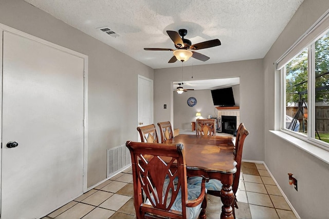 4821 Abbott Ave, Arlington, TX 76018 - dining area featuring a ceiling fan, a fireplace, light tile patterned flooring, a textured ceiling, and baseboards