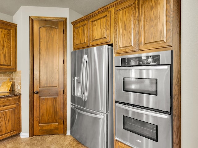 214 Crestbrook Dr, Rockwall, TX 75087 - kitchen featuring stainless steel appliances, decorative backsplash, brown cabinets, and dark stone countertops