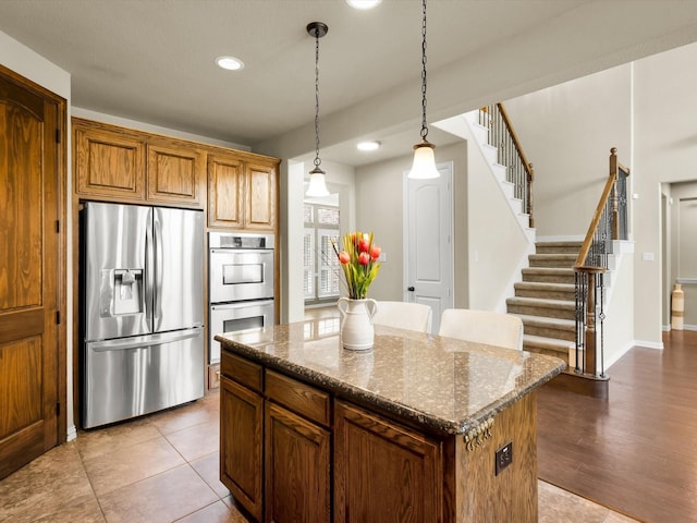 214 Crestbrook Dr, Rockwall, TX 75087 - kitchen featuring appliances with stainless steel finishes, a center island, hanging light fixtures, dark stone counters, and brown cabinets