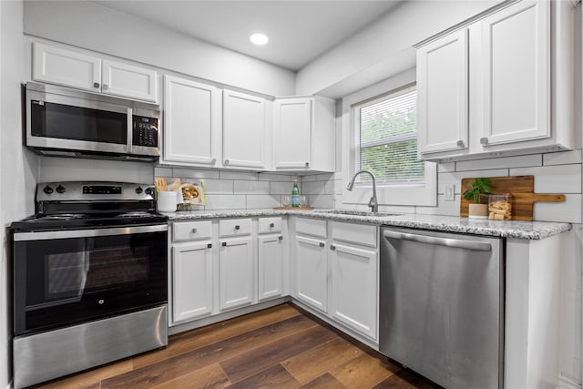 kitchen with appliances with stainless steel finishes, a sink, white cabinets, dark wood finished floors, and backsplash