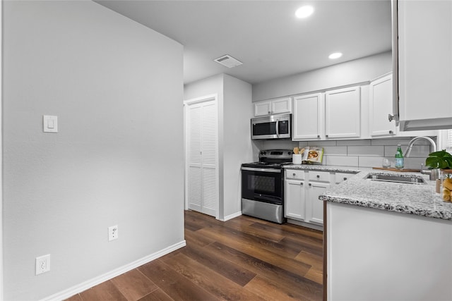 kitchen with appliances with stainless steel finishes, a sink, baseboards, white cabinets, and light stone countertops