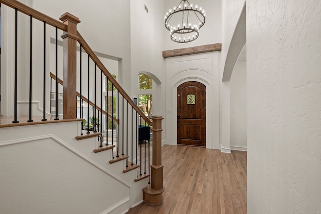 entryway with arched walkways, a chandelier, wood finished floors, baseboards, and stairway