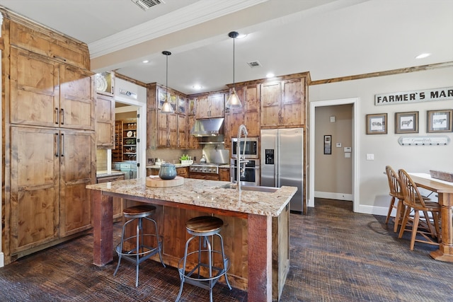 kitchen with appliances with stainless steel finishes, crown molding, light stone countertops, a center island with sink, and decorative light fixtures